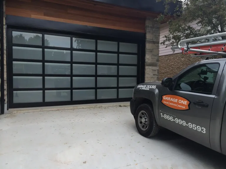 Garage One service truck parked in front of a black full-view aluminum and glass garage door